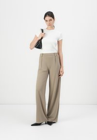 Lightweight white t-shirt paired with high-waisted, wide-leg beige trousers featuring gold button accents. Model holds a black handbag.
