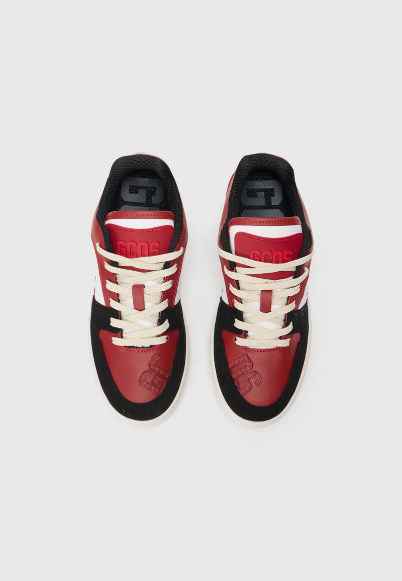 Baskets rouges et noires avec des accents blancs, présentant une tige lisse, une languette en mesh et des lacets beiges. Détail du logo embossé sur le côté.
