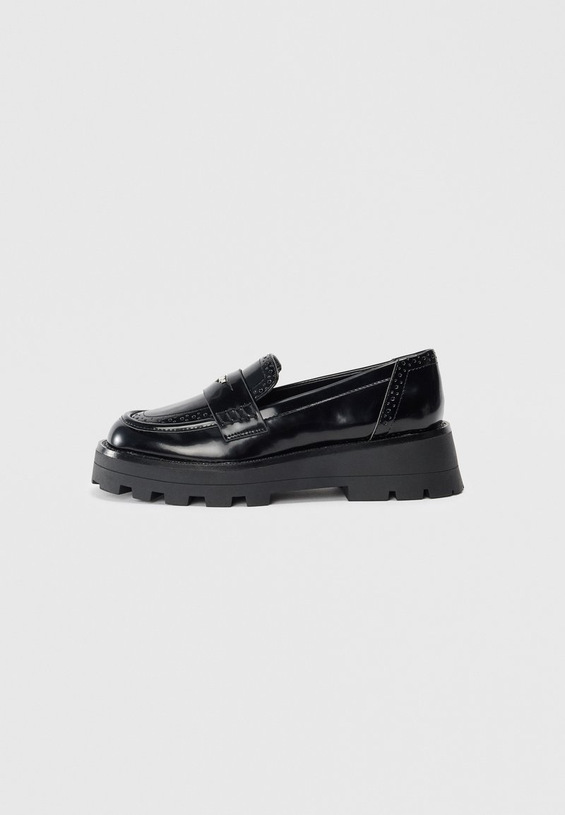 Mustad musta platvormiga loafers, millel on paks tallaga, pennistrap, dekoratiivsed perforatsioonid ja poleeritud nahkviimistlus, esitatud külgvaates.