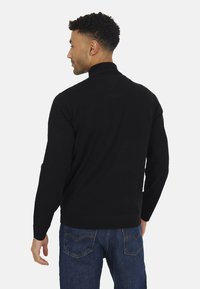 Maglione nero a maglia con colletto alto, maniche lunghe e polsini a costine, abbinato a jeans in denim blu. Design semplice e colore uniforme.