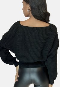 Maglione nero in maglia con scollatura ampia e vestibilità morbida, dotato di polsini e orlo a costine. Abbinato a leggings neri per un aspetto slanciato.