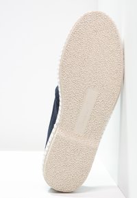 Marineblauwe stoffen sneaker met een gestructureerde witte rubberen zool, voorzien van een gladde, afgeronde neus en een versterkte hiel voor extra duurzaamheid.