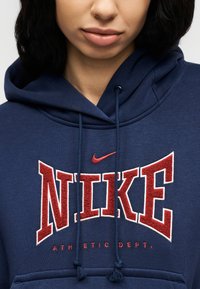 Close-up of a person wearing a navy blue hoodie with red and white "NIKE ATHLETIC DEPT." text and logo on the front.