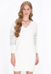 Rochie albă tricotată cu decolteu în V, cu mâneci lungi decorate cu paiete argintii și manșete și margine cu textură ribbed.