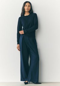 Haut à manches longues bleu marine avec des poignets côtelés, associé à un pantalon à jambes larges, également bleu marine, présentant une texture lisse et une coupe ajustée.