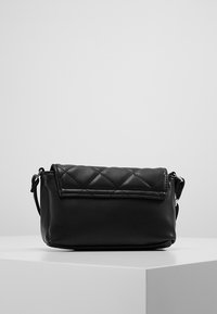 Borsa a tracolla nera con patta superiore trapuntata, realizzata in morbida ecopelle. Presenta una tracolla regolabile e un design minimalista.