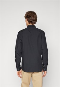 Camisa negra de manga larga hecha de algodón, con cuello estándar, puños con botones y dobladillo recto. Textura suave con un ajuste clásico.