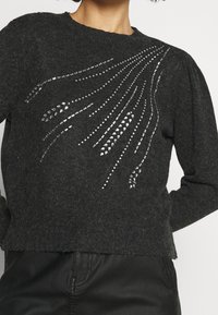 Węgielnoszary sweter z dzianiny z okrągłym dekoltem i bufkami na rękawach, ozdobiony wzorem z srebrnych ćwieków ułożonych w kaskadowy wzór.