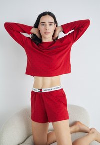 Röd tvådelad nattdräkt gjord av mjukt material, med en kortärmad topp och shorts i marinblått prickmönster samt märkeselastik.