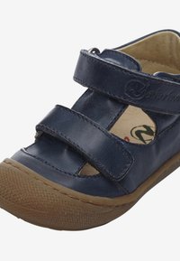 Dětské sandály v námořnické modré kůži se dvěma suchými zipy, výřezovým designem a hnědou gumovou podrážkou s texturovaným gripem.