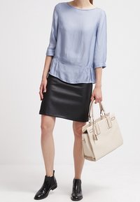 Ljusblå långärmad blus med volangslut, kombinerad med en svart imitationsläderskjol och en beige handväska. Svarta ankelskogs håller looken samman.