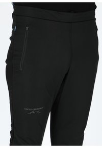 Zwarte stretchbroek met een gladde textuur, voorzien van een zijzak met rits en een logo op de dij. Inclusief een subtiele blauwe en gele accent.