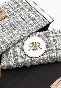 Grå och vit tweed-handväska med en rund logotyp-patch, guldfärgad hårdvara och svarta accenter; strukturerad design med texturerat tyg.