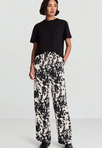 T-shirt nera con scollo rotondo abbinata a pantaloni a gamba larga con motivo schizzi bianchi e neri. I pantaloni hanno vita elastica e tasche.