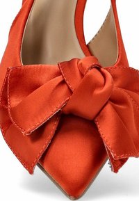 Zapato de tacón alto de satén rojo con punta afilada y un gran lazo texturizado en la parte delantera. Detalles de costura elegantes visibles.