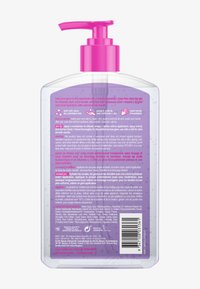 Transparent plastpumpflaska med rosa dispenser som innehåller lila självbruningsgel, detaljerade appliceringsinstruktioner och en streckkod på baksidan av etiketten.