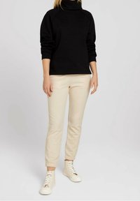 Černý rolák s dlouhými rukávy, zkombinovaný s béžovými kalhotami po kotníky a světlými šněrovacími teniskami.