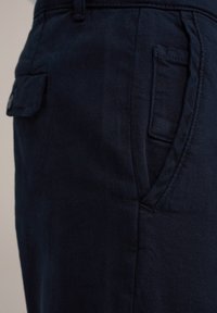 Marineblauwe broek met een gladde textuur, zijzakken en een achterzak met een klep. De stof lijkt duurzaam en iets getextureerd.