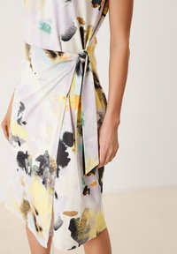 Robe multicolore avec des motifs abstraits dans des teintes pastel et des accents sombres. Détail en nœud à la taille, tissu doux avec un design drapé.