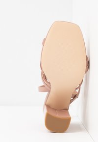 Sandale beige à talon haut avec bout carré et talon bloc, semelle tournée vers l’avant sur fond blanc.