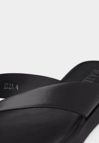 Sandale à glissière en cuir noir avec large bride et semelle texturée, présentée en gros plan sous un angle latéral.