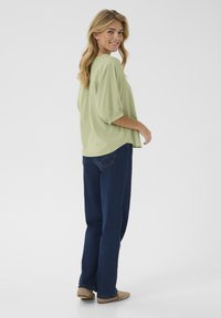 Top verde chiaro, morbido e ampio con maniche a sbuffo, abbinato a jeans a gamba dritta blu scuro e scarpe basse beige. Design semplice e informale.