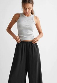 Un maiou ribat de culoare gri deschis, asortat cu pantaloni largi negri. Maioul are un decolteu rotund și design fără mâneci, în timp ce pantalonii dispun de un elastic în talie.