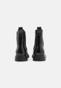 Svarta patentläder ankelstövlar med elastiska sidopaneler, drag�öglor och en kraftig sula, som har en stilren, slät yta och minimalistisk design.