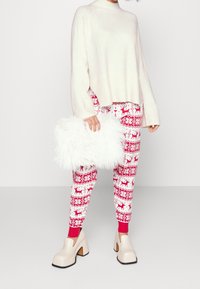 Maglione di lana lavorato a maglia, leggings rossi e bianchi con motivo renna, pochette bianca e fluffy, e scarpe con tacco a blocco beige.