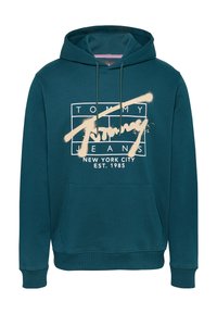 Sudadera verde azulado con un bolsillo frontal, capucha con cordones y una impresión gráfica que dice "TOMMY JEANS NEW YORK CITY EST. 1985" en color crema. Textura de tela suave.