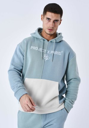 Sweatshirt à capuche en bleu clair et beige. Comprend une poche frontale, des poignets côtelés et un logo brodé sur la poitrine. Texture de tissu douce.