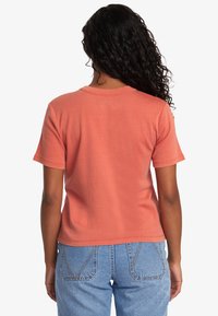 Camiseta de manga corta en color coral con un ajuste relajado, cuello redondo y material de algodón suave. Combinada con jeans de mezclilla azul claro.