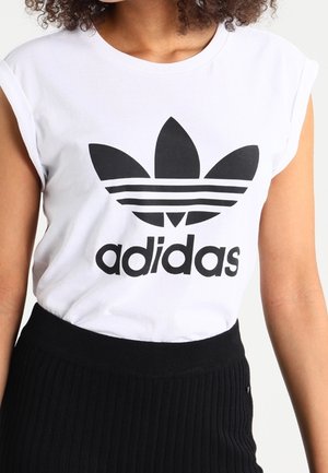 Biała bawełniana koszulka z czarnym logo Adidas i wzorem trzech pasków na piersi. Widoczne rękawki typu cap oraz okrągły dekolt. Czarny, prążkowany pas na dole.