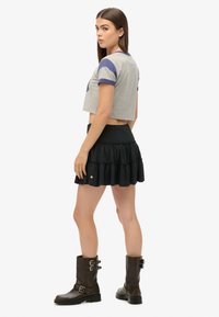 T-shirt grise courte avec accents violets, assortie à une mini-jupe noire à volants et des bottes marron montant aux genoux avec des boucles.