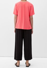Blouse rose à manches courtes avec un détail froncé dans le dos, associée à un pantalon noir à jambes larges et des sandales plates noires. Look simple, léger et décontracté.