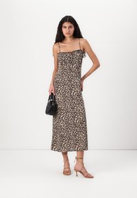 Rochie maxi cu imprimeu leopard, cu pliuri la decolteu, bretele subțiri și o siluetă subțire. Asortată cu o geantă neagră și sandale cu curele.