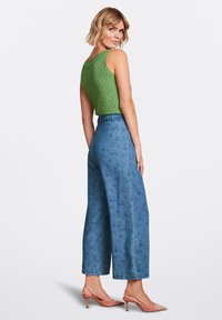Top in maglia verde, pantaloni a gamba larga blu con motivo e cintura, e tacchi a punta rosa. La texture e il colore arricchiscono l'aspetto.