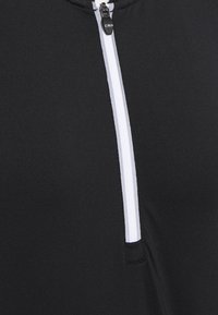 Prenda negra con cremallera que presenta una cremallera blanca, textura suave y un diseño moderno con un cuello alto y estilo minimalista.