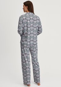 Pyjama-set met een bloemenpatroon op een lichtgrijze achtergrond. Lange mouwen, knoopsluiting op de shirt en losse broek. Zachte stof.