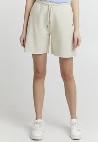 Lyse beige shorts i bomullsmiks med elastisk liv og snor, med rå kant og subtilt logodesign på siden.