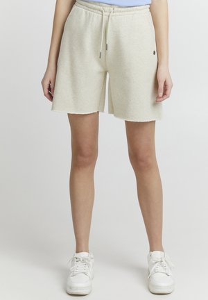 Lyse beige shorts i bomullsmiks med elastisk liv og snor, med rå kant og subtilt logodesign på siden.