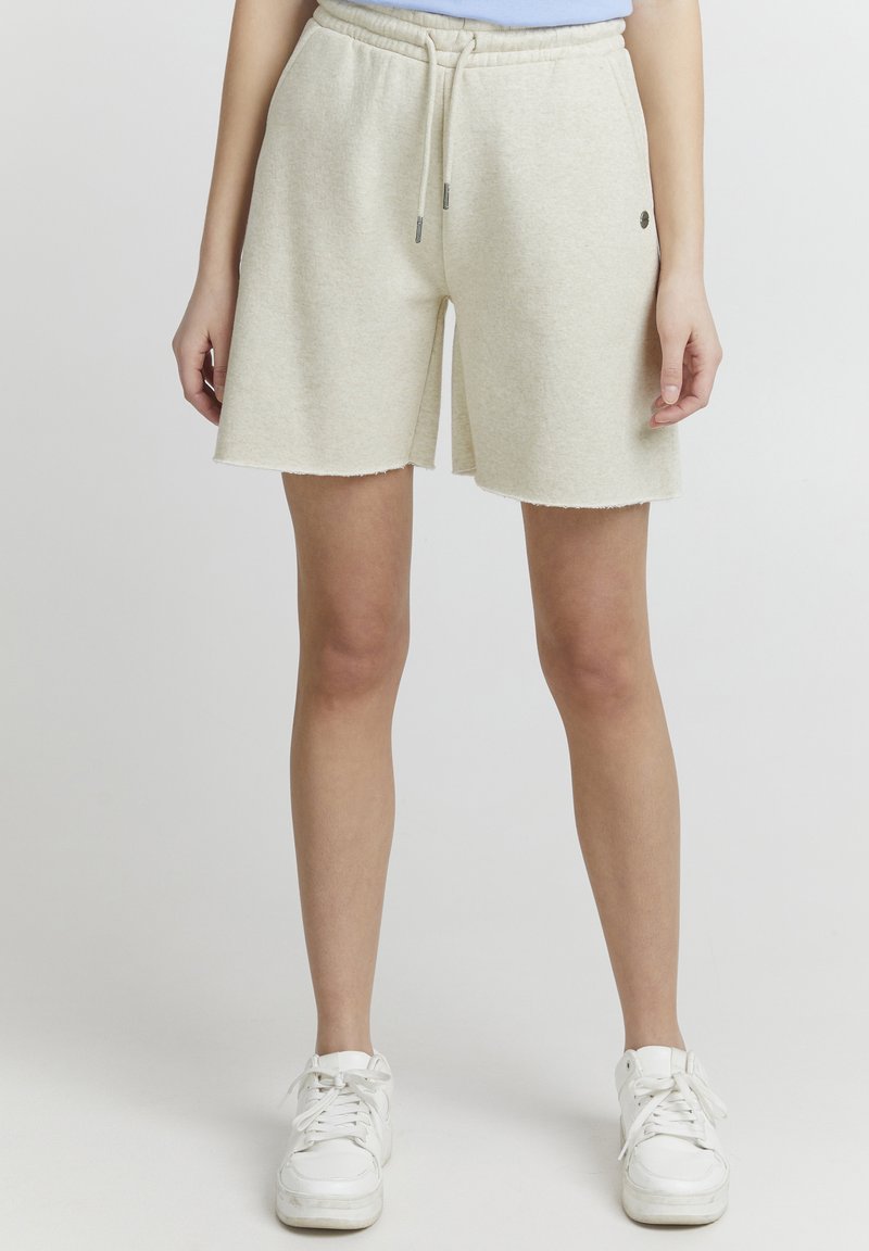 Lyse beige shorts i bomullsmiks med elastisk liv og snor, med rå kant og subtilt logodesign på siden.