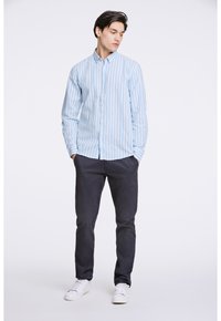Camisa de manga larga a rayas azul claro y blanca con cuello abotonado, combinada con pantalones azul oscuro y zapatillas deportivas blancas. Textura de tela suave.