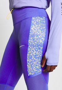 Fialové sportovní legíny mají strukturovanou látku, barevně vzorovanou boční panel a hladký pas s detailem na stažení.