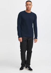 Navy textured crew-neck sweater, fitted silhouette, paired with black slim-fit pants and black sneakers with white stripes.