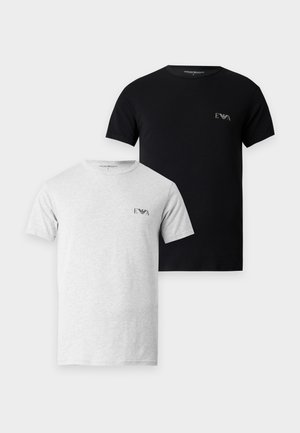 Homme debout pieds nus portant un t-shirt noir ajusté à manches courtes et un boxer vert sur un fond blanc uni.