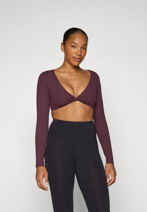 Haut cropped à manches longues bordeaux avec un décolleté en V profond et un détail à l'avant tordu, associé à un legging noir taille haute. Texture lisse.
