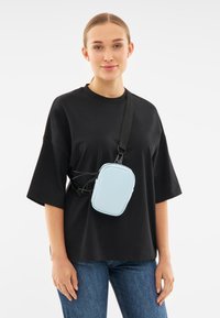 Borsa a tracolla blu chiaro realizzata in materiale liscia, forma rettangolare, chiusura con zip, con tracolla nera regolabile e dettagli elastici.
