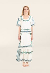 Weißes Zwei-Teiler-Outfit mit blauer und grüner floraler Stickerei, bestehend aus einem lockeren Oberteil mit kurzen Ärmeln und einem bodenlangen, gestuften Rock.
