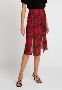 Röd ormtryckt midi kjol med sidoslitsar, lätt material, åtsittande midja och en flödande silhuett. Kombineras med svarta remsandaler.